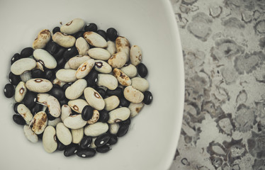 Several types of beans in a white pot on a marble surface