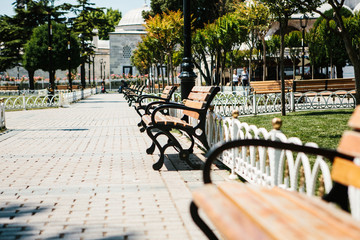 Fototapeta na wymiar Benches in sunny park with alleys against background of trees. Sultanahmet Square in Istanbul. Public space.
