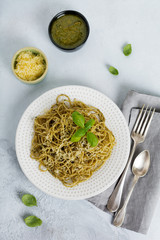 Pasta spaghetti with pesto sauce, basil and parmesan cheese on a white ceramic plate and gray concrete or stone background. Traditional Italian dish. Selective focus. Top view.