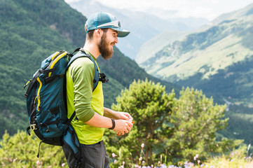 Portrait of a young traveler with a beard and a backpack in a cap and sunglasses against the background of the Caucasus Mountains