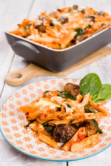 Easy one pot penne pasta oven dish with meatballs, spinach, pecorino, mozzarella cheese and tomato sauce. Served on a vintage orange plate with white wooden background. Selective focus.