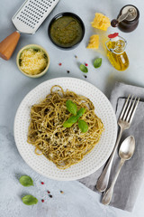 Pasta spaghetti with pesto sauce, basil and parmesan cheese on a white ceramic plate and gray concrete or stone background. Traditional Italian dish. Selective focus. Top view.