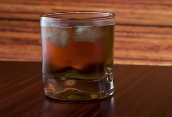 Glass of wiskey and ice on wooden background