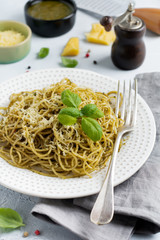 Pasta spaghetti with pesto sauce, basil and parmesan cheese on a white ceramic plate and gray concrete or stone background. Traditional Italian dish. Selective focus. Top view.