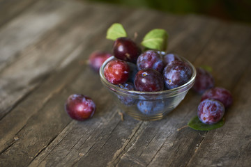 Fresh plums in plate on wooden background