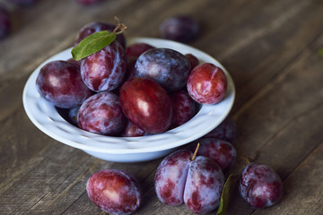 Fresh plums in plate on wooden background