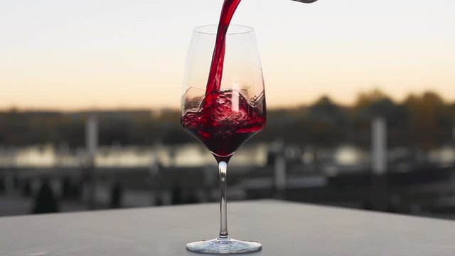 Red wine is poured to the wineglass outdoors in slow motion, bar and restaurant, alcohol drinks, food in slow motion, 240 frames per second