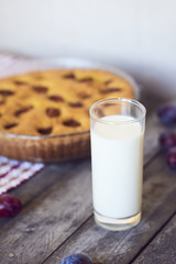Glass of milk with homemade plum pie on rustic background