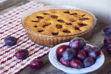homemade plum pie with fresh plums in plate on rustic background