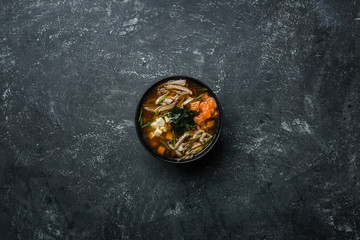Japanese miso soup with tofu and salmon in a black bowl on a vintage colored background. Vertical...