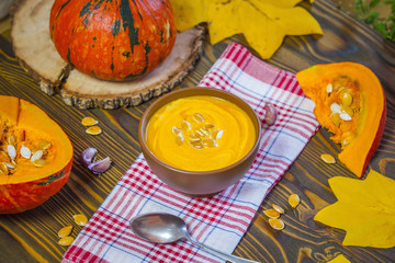 Pumpkin cream soup with cream and pumpkin seeds on wooden background, selective focus