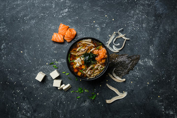 Japanese miso soup with tofu and salmon in a black bowl on a vintage colored background with...