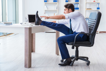 Young businessman doing sports stretching at workplace