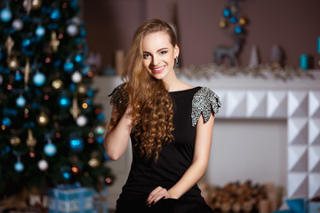 Holidays, celebration and people concept - young woman in elegant dress over christmas interior background