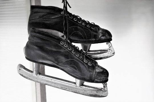 vintage pair of mens ice skates hanging on a wooden wall in black and white color