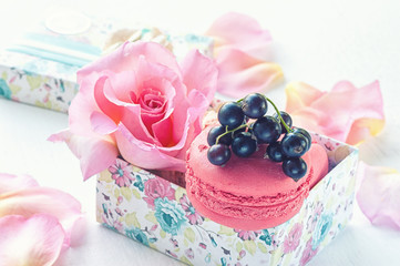 Macarons with black currant in a gift box on the background of beautiful flowers roses. Dessert close-up.