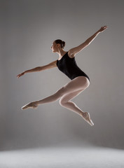 Fototapeta na wymiar Elegant ballerina in black tights and pointes soars in the air