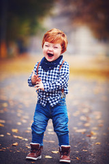 happy laughing toddler baby boy with red hair having fun at autumn park