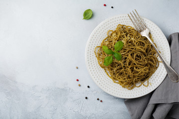 Pasta spaghetti with pesto sauce, basil and parmesan cheese on a white ceramic plate and gray concrete or stone background. Traditional Italian dish. Selective focus. Top view.