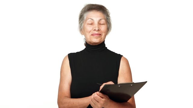 picture of elderly businesswoman with white temples holding clipboard looking at camera nodding with smile over white background. Concept of emotions