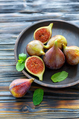 Ripe figs and mint leaves on a wooden dish.