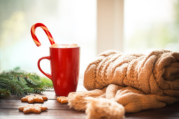 Christmas gingerbread, candy, coffee with marshmallows in red cup, knitted scarf, cones  and christmas tree branches on wooden table on window background. Xmas holidays background, winter home cozy