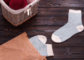 Knitted socks and basket with yarn on wooden background