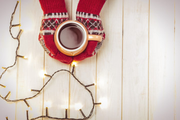 A cup of hot tea, a drink in mittens. Christmas concept. New Year's decor. Garlands