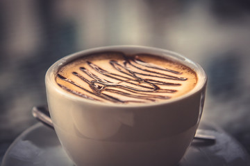 cup of fragrant coffee cappuccino with syrup on blurred background in vintage style in warm colors