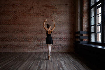 People, art, theatre, choreoography and dance concept. Back view of slender beautiful young ballerina in black dress standing en pointes in the middle of ballet studio, practicing center work