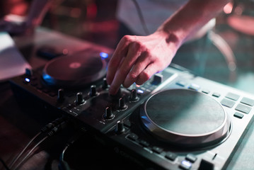 Hands of man DJ tweak various track controls on dj's deck at night club 