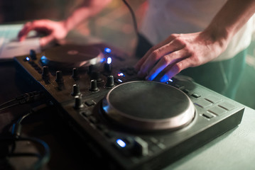Fototapeta na wymiar Hands of man DJ tweak various track controls on dj's deck at night club 
