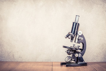 Retro old scientific laboratory microscope circa 40s on wooden table front concrete wall...