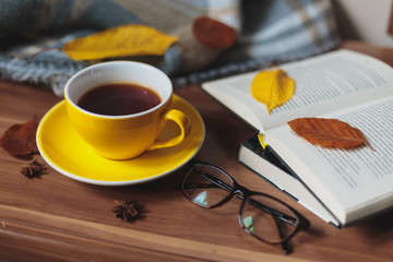 Autumn mood. Yellow cup with hot tea and book on the wooden surface.