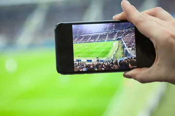 Foto op Canvas Cellular phone screen with football stadium field with teams playing game © Kekyalyaynen