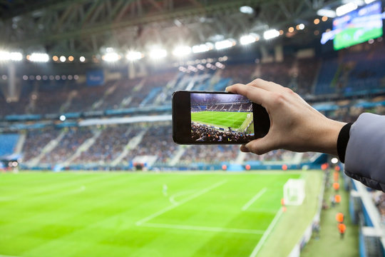 Fan hand with smartphone photographing footbal game