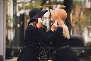 Fashionable women friends in hat make kiss gesture to each other