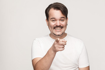 The happiness man, wearing white tshirt, having happiness looks, pointing finger at camera and toothy smiling.