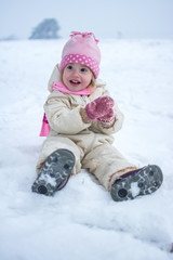 Fototapeta na wymiar Little girl sitting on snow in winter park.