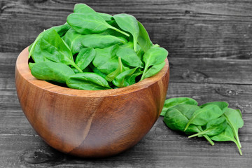 Green baby spinach leaves in a wooden bowl
