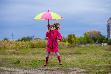 Colorful umbrella cute girl jump funny to sky. Small cheerful girl walks with an umbrella in the rain
