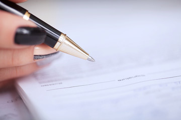 Business woman sitting at office desk signing a contract with shallow focus on signature.