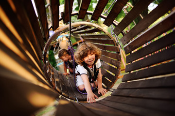 cute children - a boy and a girl in an adventure park are engaged in rock climbing or pass obstacles on the rope road.
