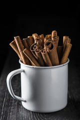 Taza de porcelana con palitos de canela en rama sobre fondo de madera negro