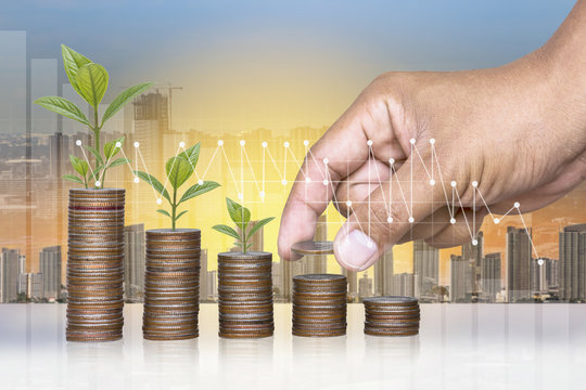 Hand stacking gold coins with seedlings are growing on coins laid out and blurred building background,Business Finance and Money and Save money for prepare in the future,productivity growth concept