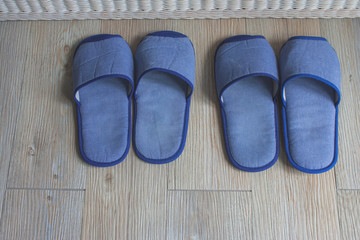 Top view blue comfortable slippers two pairs on wooden floor in the bedroom.