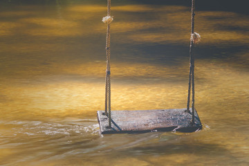 Relaxation Concept : Wooden swing hanging on tree above the water stream at outside resort in vintage style. (Soft focus)