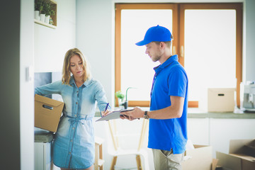 Obraz premium Smiling delivery man in blue uniform delivering parcel box to recipient - courier service concept. Smiling delivery man in blue uniform