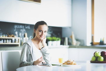 Young woman with orange juice and tablet in kitchen.