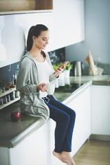 Woman using mobile phone sitting in modern kitchen.
